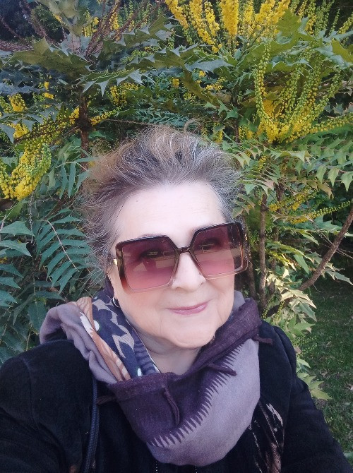 Женщина в темных очках на фоне растительности с желтыми цветами