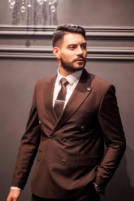 Мужчина в элегантном коричневом костюме позирует на фоне серой стены