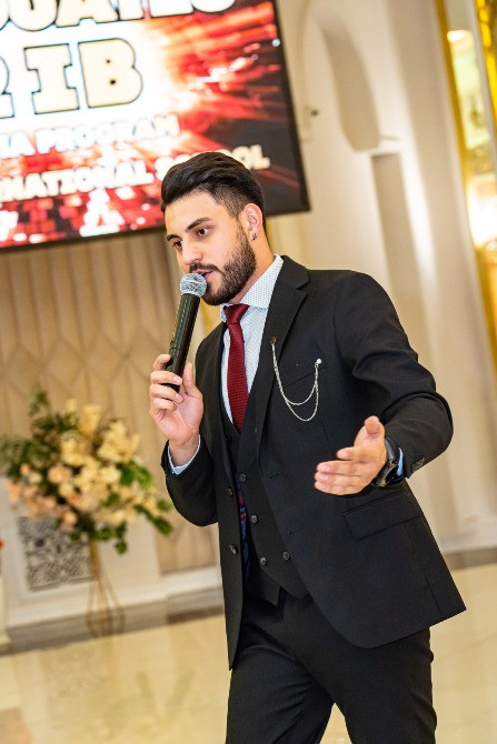 Мужчина в костюме с микрофоном, объясняет что-то аудитории в торжественной обстановке