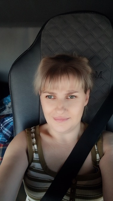 Қысқа шашты әйел автокөліктің жүргізуші сиденьесінде, ақ былғары өңдеу мен жұмсақ жарықпен отыр.