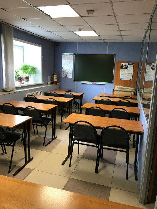 Классная комната с партами и стульями, окна с растениями