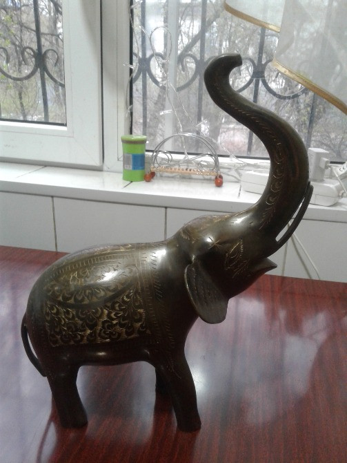 Жоғары көтерілген хоботы бар қоладан жасалған піл фигурасы, ағаш бетінде орналасқан.