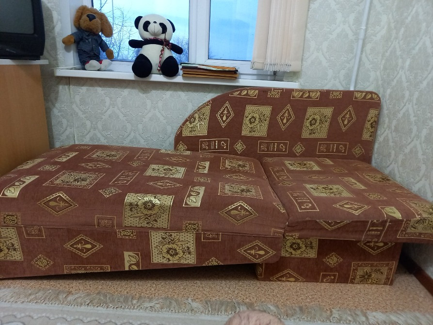 Диван с декоративным текстилем в коричневых и золотых тонах, расположенный у окна, рядом с мягкими игрушками