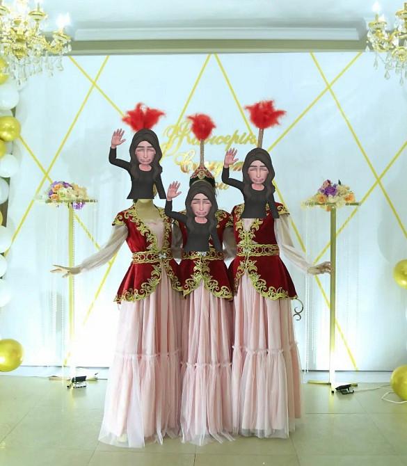 На изображении изображены три женщины в костюмах, стоящие на фоне праздничного оформления с золотыми шарами и красными аксессуарами