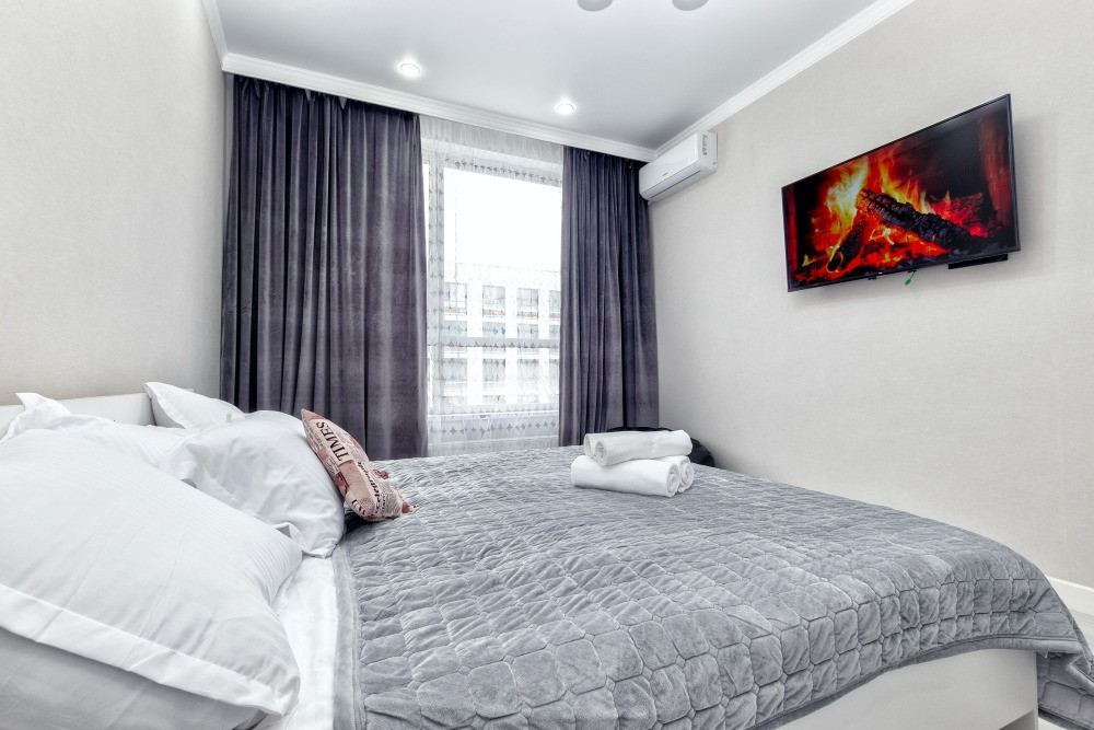 Современная спальня с постельным бельем и телевизором на стене