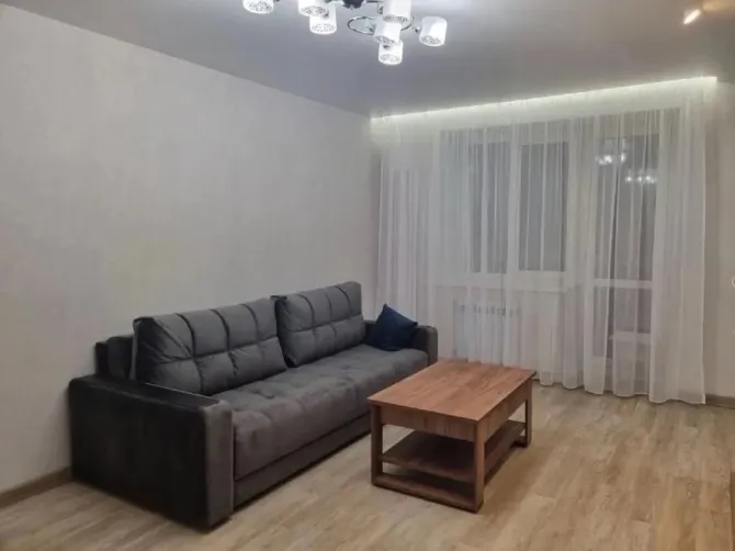 Уютты қонақ бөлме диванмен және үстелмен, үлкен терезелерімен