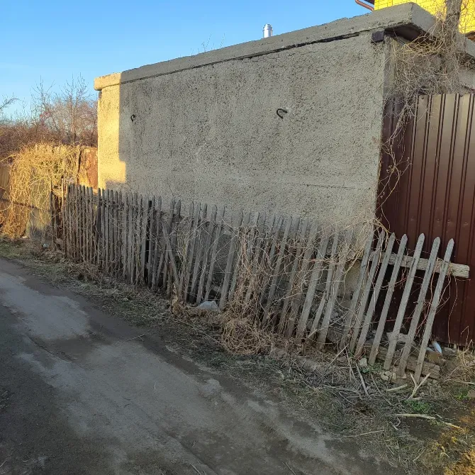 Старый дом с бетонными стенами и забором из деревянных палок