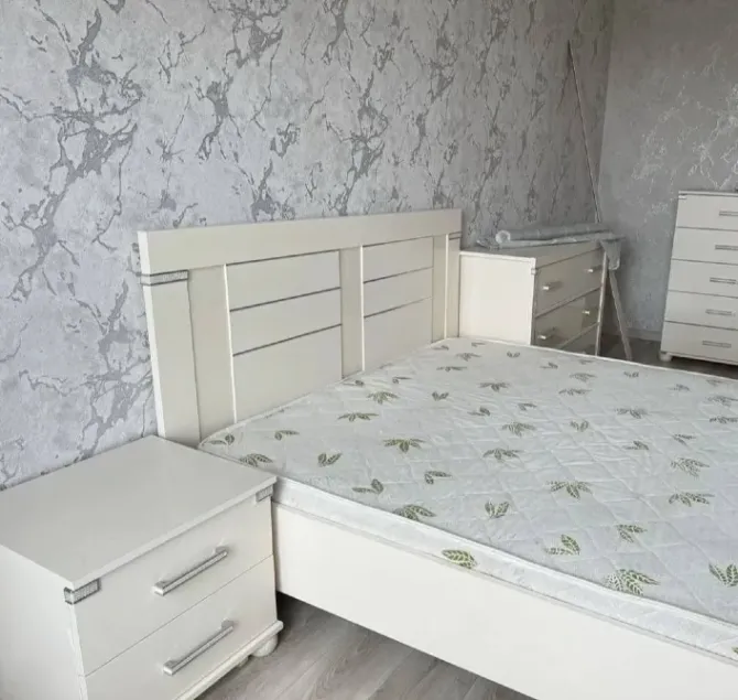 Ақ төсек пен комод фонында орналасқан ұйықтау бөлмесі