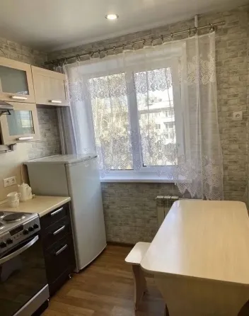 Кухня с холодильником, плитой и обеденным столом рядом с окном