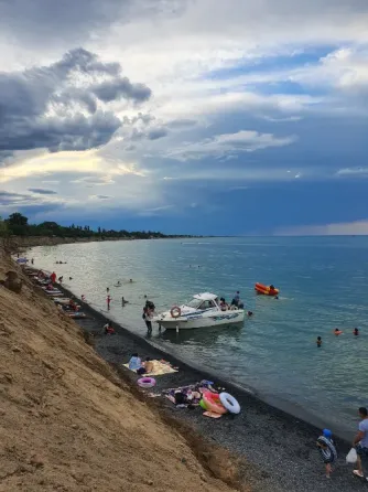 Нөсерлі бұлттардың фонында адамдар мен катері бар жағажай
