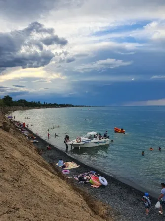 Пляж с людьми и катером на фоне грозовых облаков