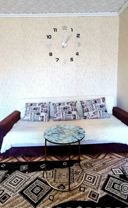 Уютный диван с подушками и круглым столиком на фоне настенных часов