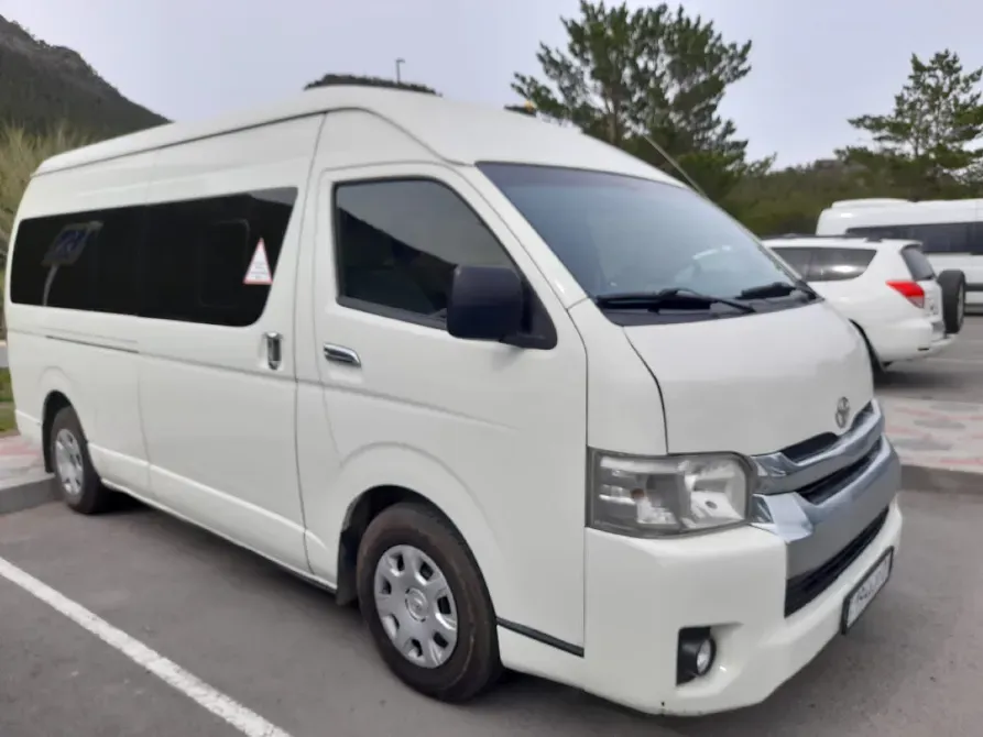 Белый микроавтобус Toyota на парковке с деревьями на фоне