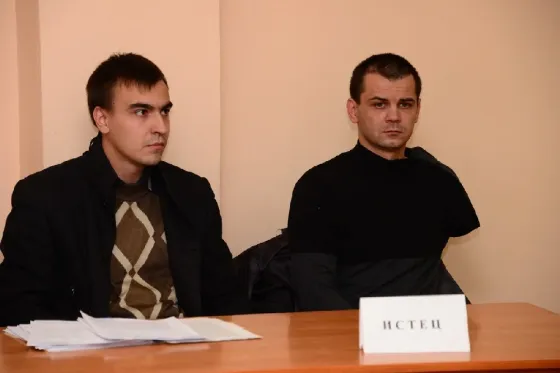 Два человека сидят за столом, один из них выглядит серьезным, документы на столе