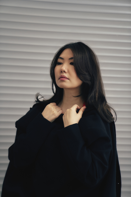 Ұзын шашы бар әйел қара плащымен, киімін түзетіп жатқан сәтте түсірілген