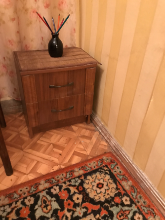 Маленький комод с цветными ручками и вазой с карандашами на фоне полосатых стен