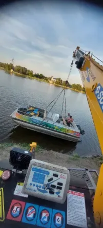 Кран поднимает лодку на реке с двумя людьми на борту