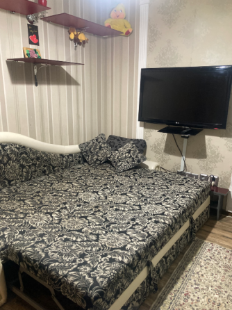 Диванмен, жастықтармен және қабырғаға орнатылған телевизормен жабдықталған бөлме