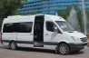 Жасыл парк пен фонтанының фонында ашық есіктері бар Mercedes-Benz ақ микроавтобусы