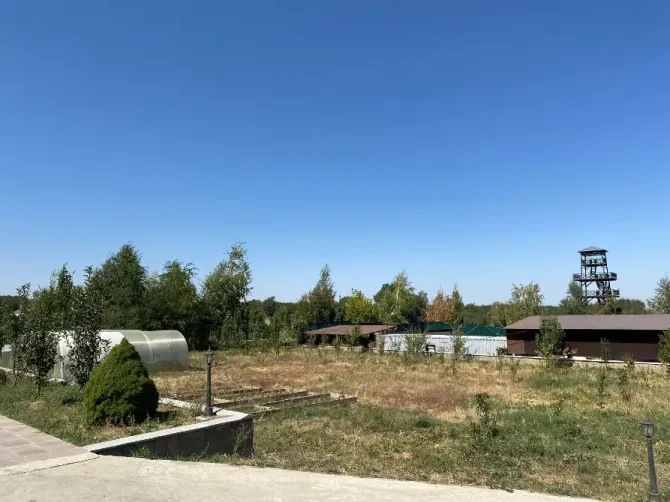 Жасыл ағаштардың фонында жылыжай мен учаскесі бар пейзаж