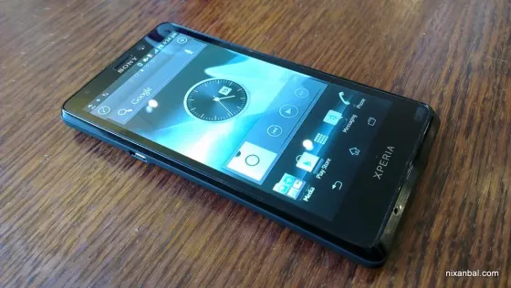 Смартфон Sony Xperia на деревянной поверхности, экран с часами и значками приложений