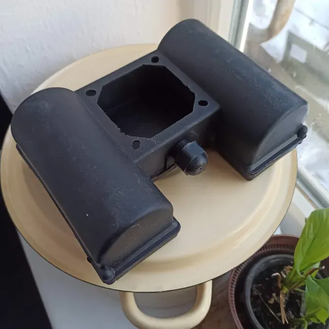 Қара пластикалық элемент, мүмкін, механизмнің бөлшегі, үстелдің үстінде өсімдікпен қатар орналасқан