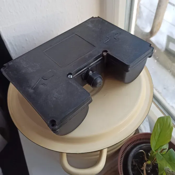 Қара пластикалық элементтің екінші жағынан көрініс, мүмкін, үстелде орнатылған механизмнің бөлшегі