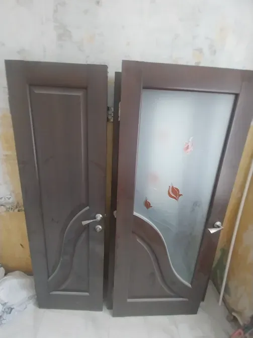 Две деревянные двери, одна из которых с прозрачной стеклянной вставкой, на фоне стены с обоями, частично отклеившимися