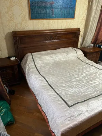 Вид на двуспальную кровать с шелковым покрывалом, рядом с ночными столиками