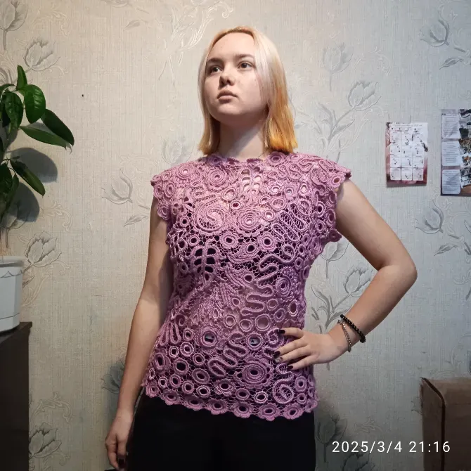 Женщина в лиловой кружевной блузке на фоне стены с растениями