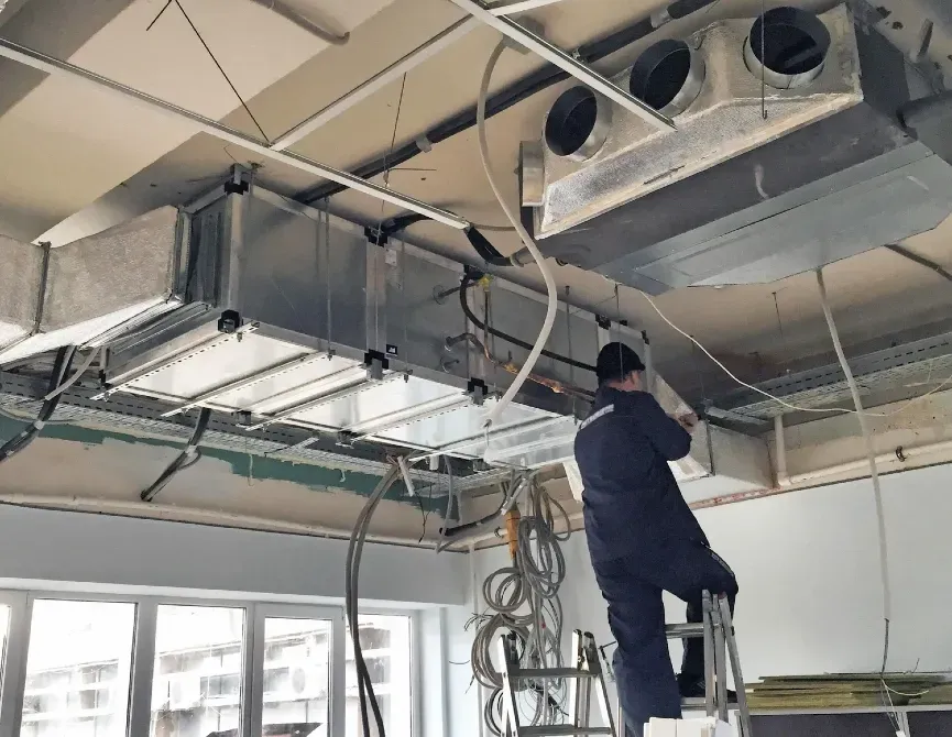 Монтаж вентиляционных систем в помещении с профессионалом, работающим на лестнице