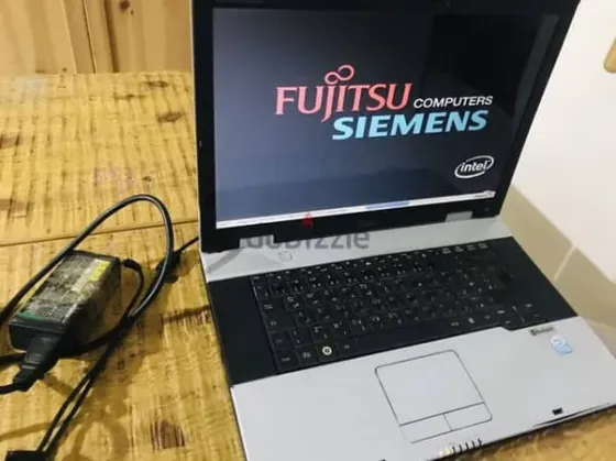 Ноутбук Fujitsu Siemens с включённым экраном на фоне логотипа и подключённым блоком питания