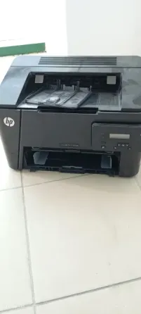 Принтер HP, черного цвета, стоит на плиточном полу с открытым лотком для бумаги