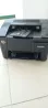 HP принтері, қара түсті, плитка еденінде ашық қағаз лоткасымен тұрған.