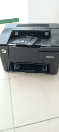 Принтер HP, черного цвета, стоит на плиточном полу с открытым лотком для бумаги