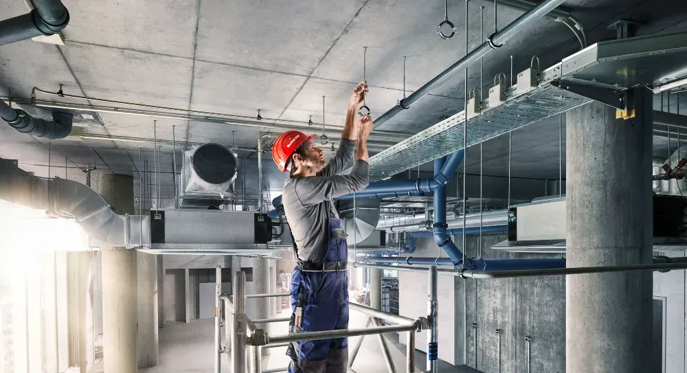 Рабочий в каске устанавливает системы вентиляции на высоте в незавершённом здании