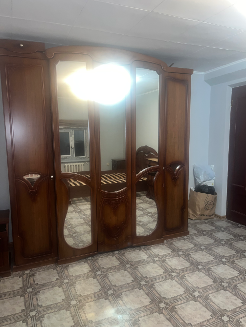 Шкаф с зеркалами и кровать в спальне при искусственном освещении