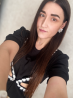 Ұзын шашы бар жас әйел, гүлдермен безендірілген қара көйлек киіп, селфи жасап тұр. Оның қамқорланған қастары мен сырғалары, күлімсіреп тұрғаны айқын с