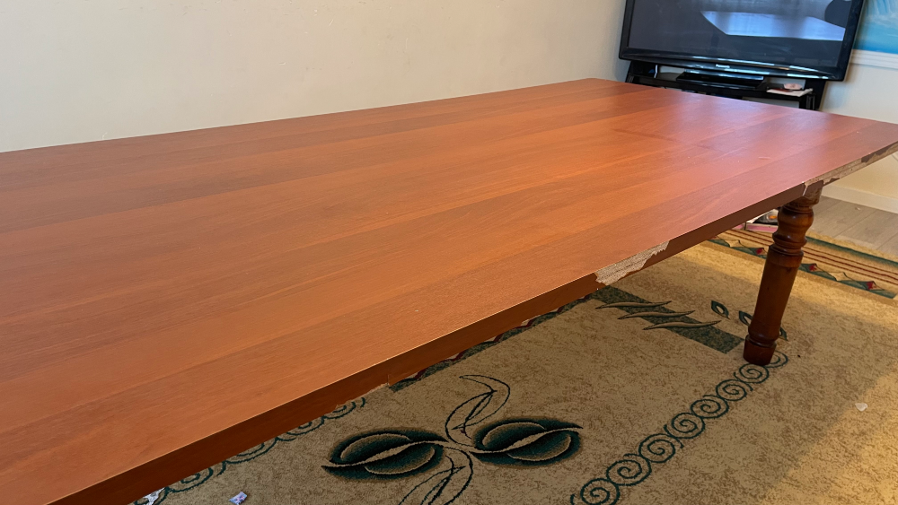 Ағаш үстелдің зақымдалған жиегі және интерьерде кілем жабыны.