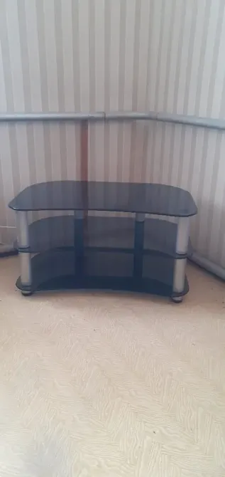 Угловой стеклянный стол с полками, оформленный в минималистичном стиле. Столешница черного цвета, каркас из металла. Подходит для размещения телевизора или аудиоаппаратуры