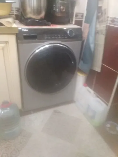 Стиральная машина с фронтальной загрузкой в кухне, рядом с пластиковыми бутылками и посудой