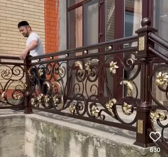 Рабочий устанавливает кованое ограждение с золотыми элементами на балконе