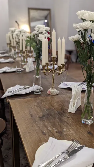 Длинный стол с белыми цветами и свечами в центре, оформленный для торжественного мероприятия