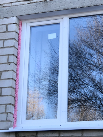 Окно с белой рамой на кирпичном доме, отражающее окружающую природу