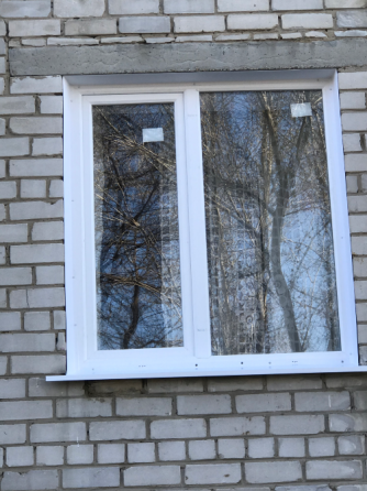 Окно с белой рамой на кирпичном доме с отражением деревьев