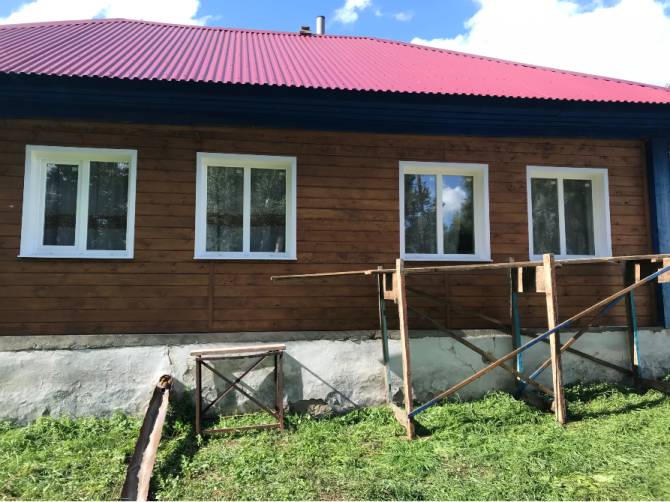 Фасад дома с белыми окнами и красной крышей на фоне зелени