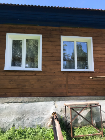 Два окна с белыми рамами на деревянном фасаде дома