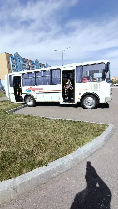 Жолдағы ақ автобус, ашық есігімен, іште адамдар