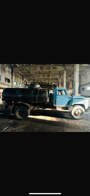 Грузовик с баком, стоящий в тёмном цехе, с освещением, падающим через окна