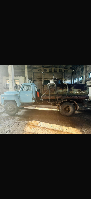 Грузовик с баком, установленным сзади, на фоне плохо освещённого помещения